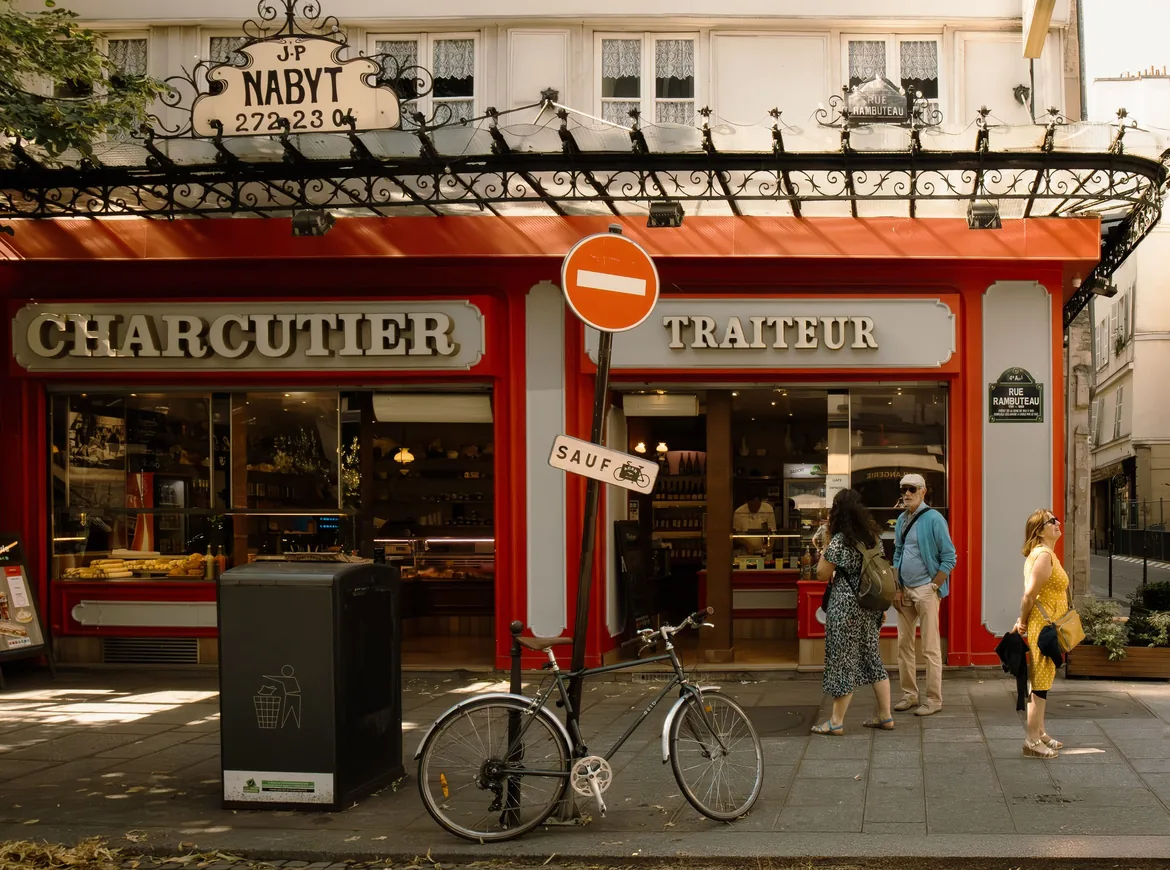 A red-fronted Paris charcutier and traiteur with a bicycle propped outside and shoppers on the pavement