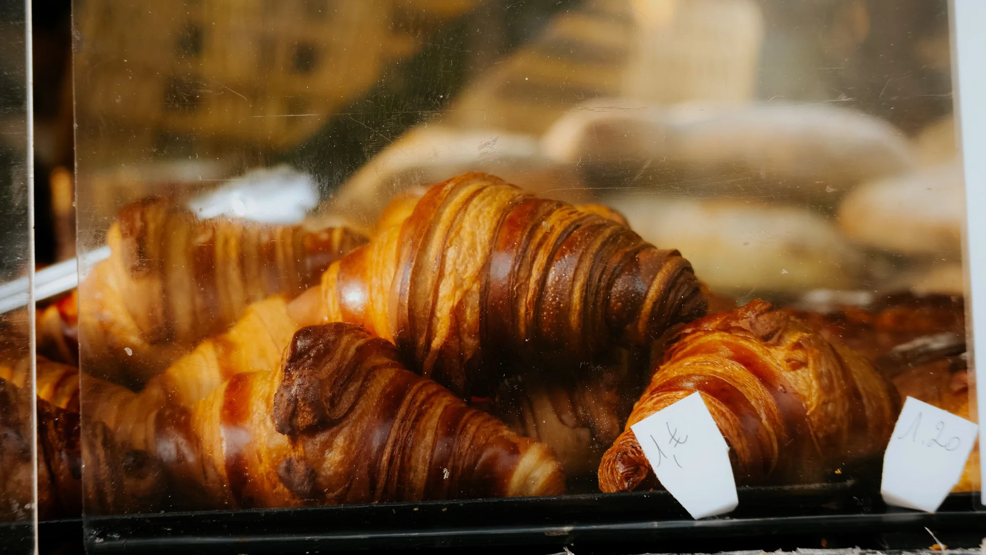 Golden butter croissants stacked behind the glass of a bakery display case