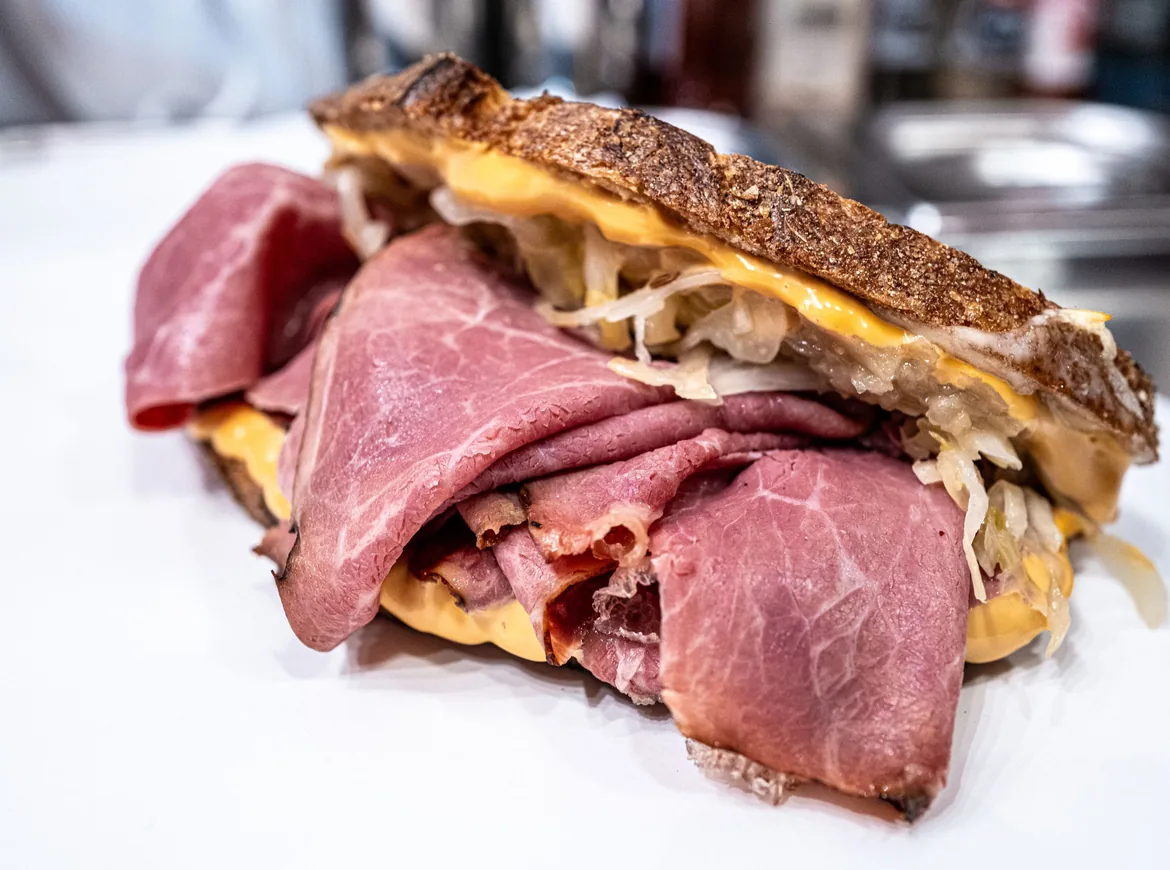 A toasted sandwich piled with thin slices of pink pastrami, melted cheese and sauerkraut